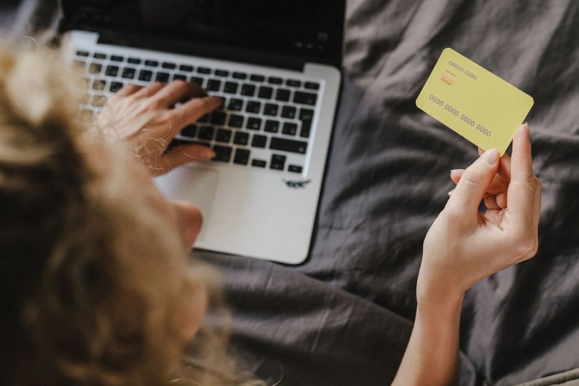 woman holding a yellow credit card using a laptop